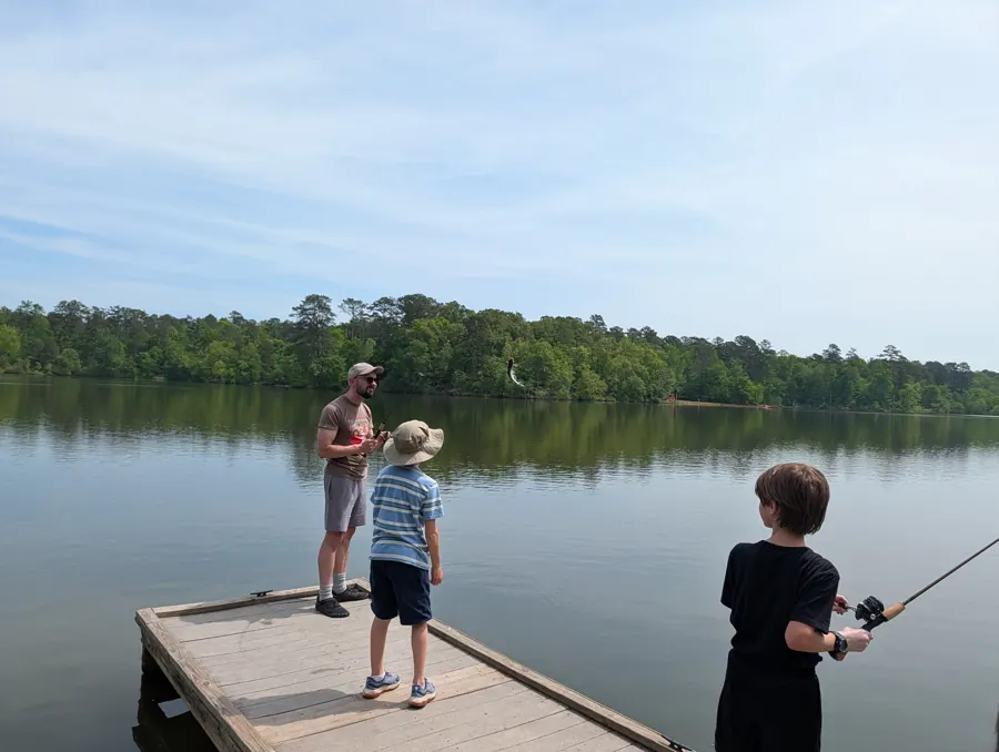 An adult leader and two boys fishing from a dock at Hard Labor Creek